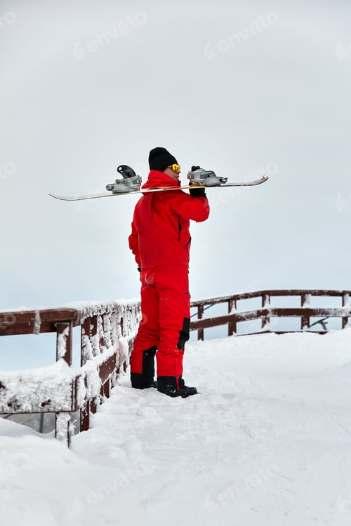 Preview: Male snowboarder in a red suit walking on the snowy hill with snowboard, Skiing and snowboarding