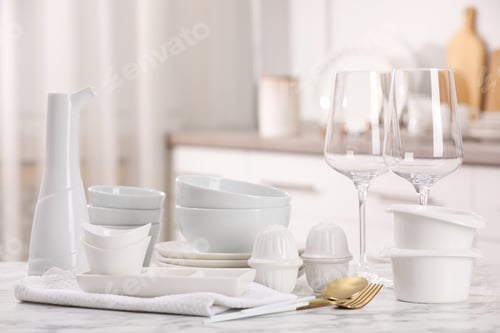 Preview: Different clean white dishware, glasses and cutlery on marble table indoors