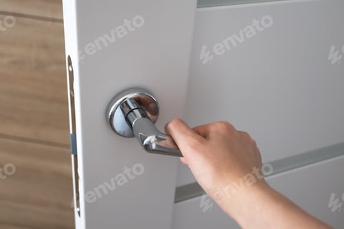 Preview: Woman hand pushing on metal door handle opening door in bedroom, close-up