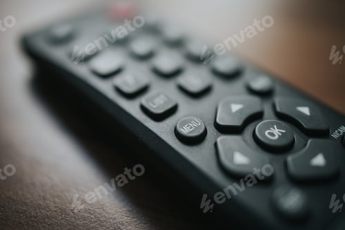 Preview: Selective focus shot of a black remote control for the TV with buttons on the wooden background.