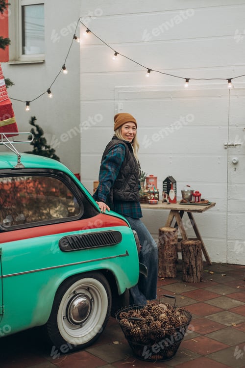 Preview: Young blonde woman near retro car with Christmas decorations