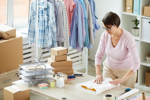Preview: Young brunette woman packing folded casualwear into paper