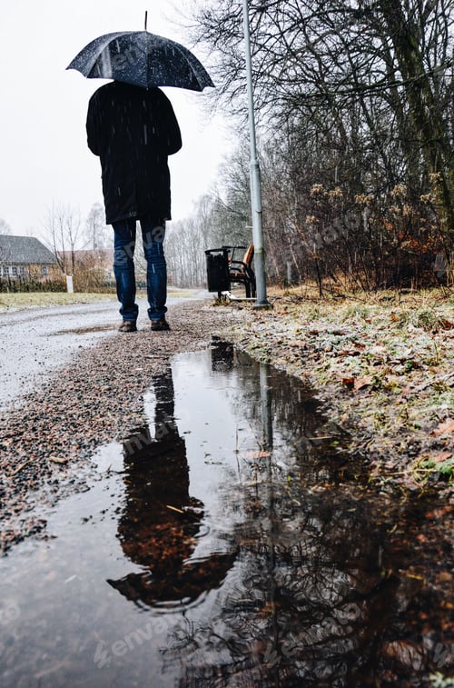 Preview: A man holding an umbrella reflected in water puddle