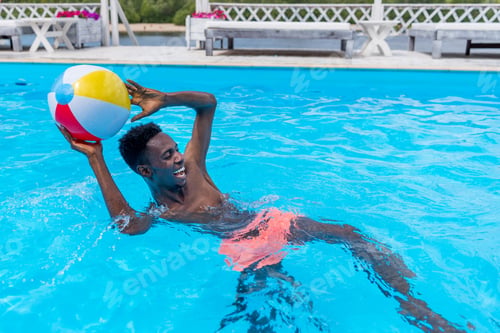 Preview: Young happy african american man playing with ball in swimming pool