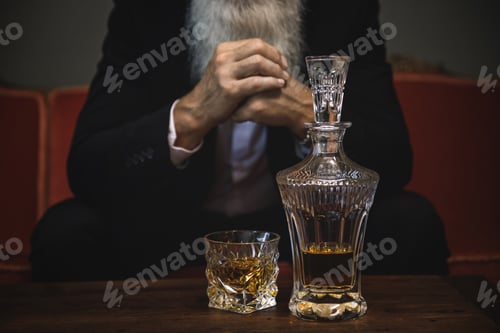 Preview: Handsome and bearded senior man drinking whiskey