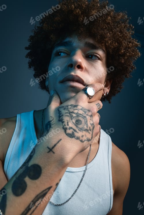 Preview: Cool young tattooed ethnic guy touching chin in studio