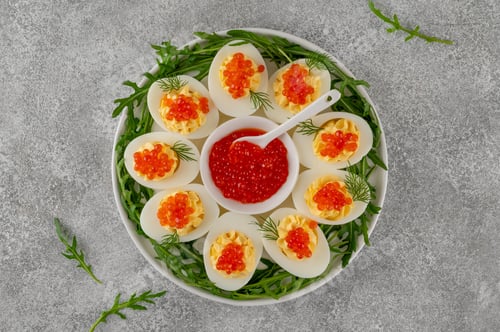 Preview: Christmas appetizer. Deviled eggs topped with red caviar on a white plate. Festive party snack