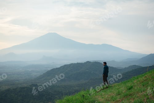 Preview: Man standing on the hills with the view of a valley and mountains in front of him