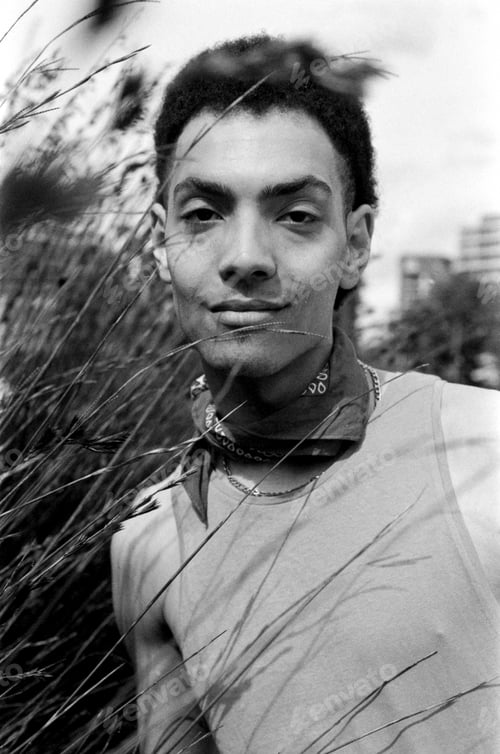 Preview: Young man wearing bandana posing behind grass in monochrome analog photo