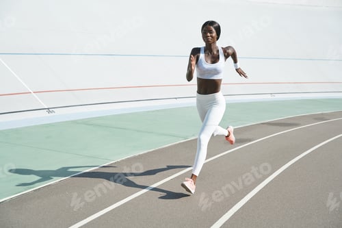 Preview: Beautiful young African woman in sports clothing running on track outdoors