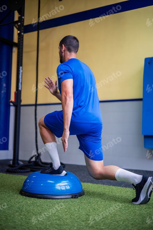 Preview: young fitness athlete doing leg strength and balance exercises with Bosu ball in gym