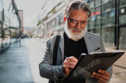 Preview: Senior business man standing outside and taking notes on a clipboard
