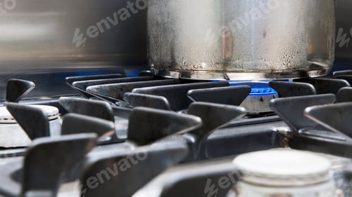 Preview: Close up of a metal pan on a gas hob, blue flames heating the pan.