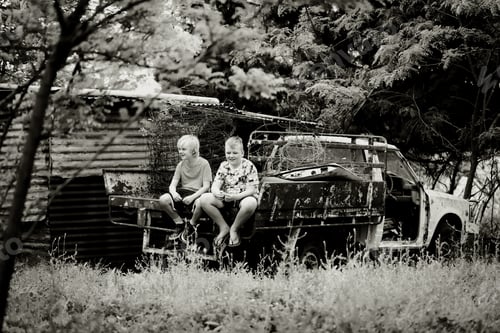 Preview: Grayscale shot of little boys playing together in a vibrant field at sunset