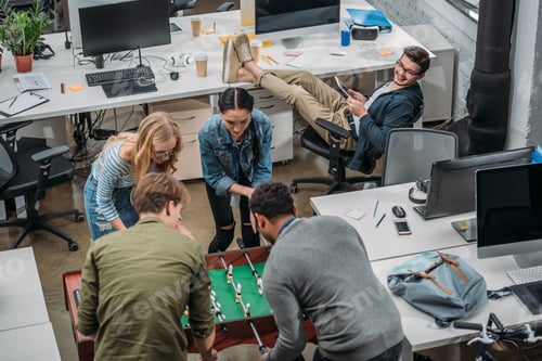 Preview: multiethnic colleagues playing in table soccer at modern office