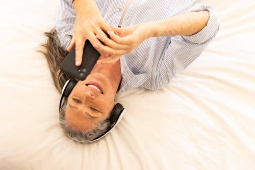Preview: Listening to music with headphones, woman lying on bed using smartphone