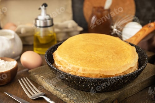 Preview: Delicious homemade crepes or pancakes in a frying pan and ingredients on a rustic table.