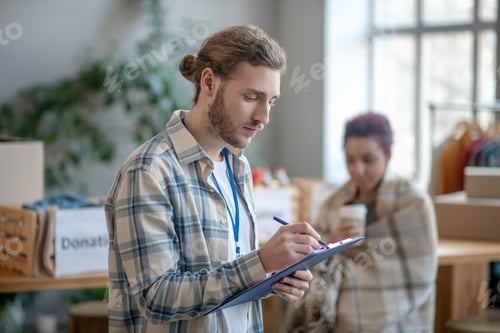 Preview: Young busy man standing indoors at work and writing.
