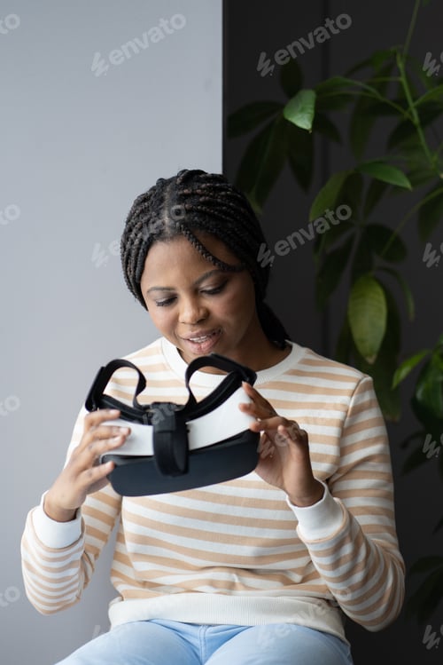 Preview: Vr goggles for gaming, shopping or work. Young african woman hold virtual reality glasses at home