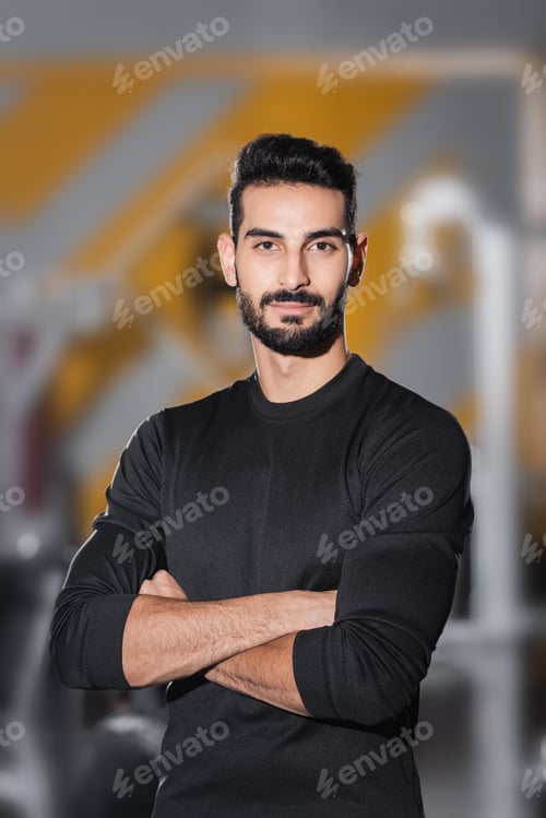 Preview: Bearded arabian sportsman looking at camera in blurred sports center