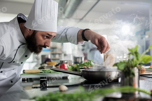 Preview: Food industry worker preparing ingredients for meal while seasoning vegetable stew with herbs and