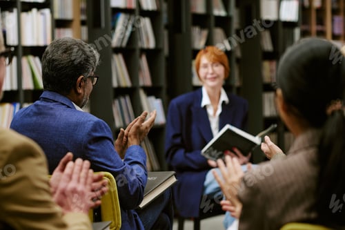 Preview: Middle Aged Caucasian Woman Presenting Book to Diverse Audience in Library