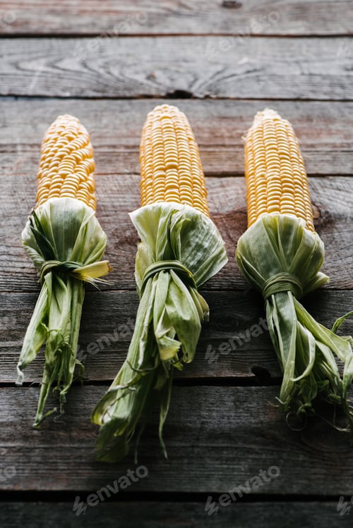 Preview: close up view of fresh raw corn cobs arranged on wooden surface