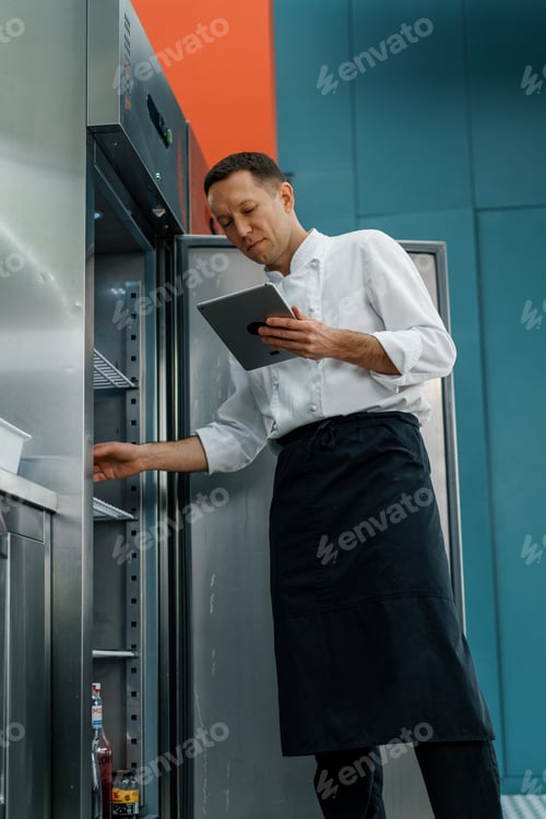 Preview: Professional chef using tablet computer for recipes while working in modern kitchen cooking concept