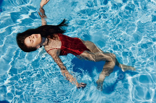 Preview: Young woman in the pool in red swimsuit with a beautiful smile lying on the water and swimming in