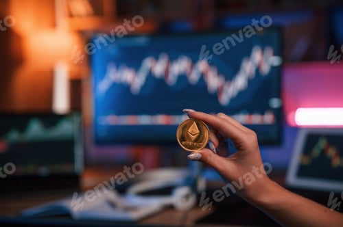 Preview: Close up view of woman's hand that holding bitcoin against computer display and tablet with graphs