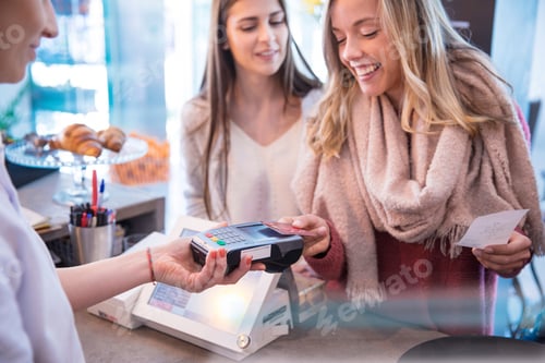 Preview: Female friends standing at counter in cafe, paying using credit card