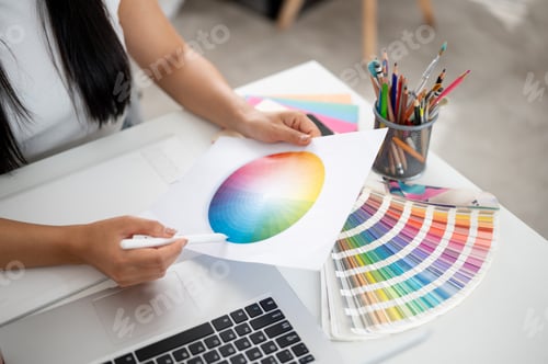 Preview: A close up of hand holding a circle color chart and a stylus pointing at blue color on working table