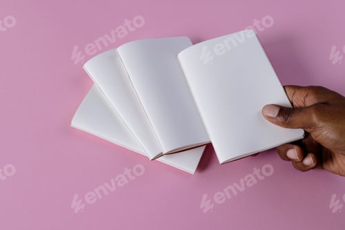 Preview: Hand of biracial man holding notebook over notebooks with copy space on pink background