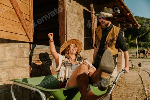 Preview: Young happy farmer couple having fun with wheelbarrow at ranch.