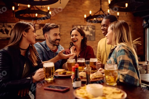 Preview: Cheerful group of friends talking while drinking beer in a bar.