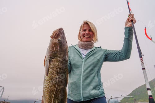 Preview: Happy Fisherwoman holding big arctic cod. Norway happy fishing. Woman with cod fish in hands