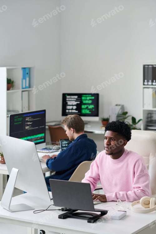 Preview: Young Black Man Working on Computer in Office with Colleague Coding