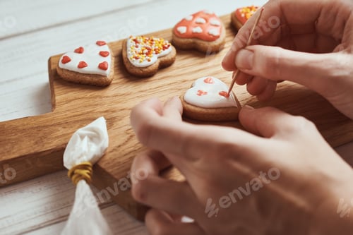 Preview: Decorating gingerbread cookies with icing. Woman hand decorate cookies in shape of heart, closeup