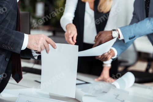 Preview: cropped view of businesswoman pointing with finger at blank paper near partners