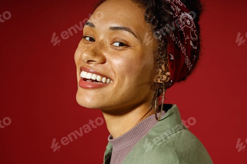 Preview: Close up of charming woman looks camera with smile while posing on red studio background