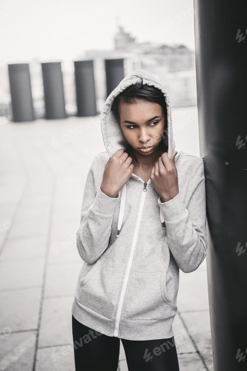 Preview: Attractive young sportswoman in hood posing on stadium and looking away