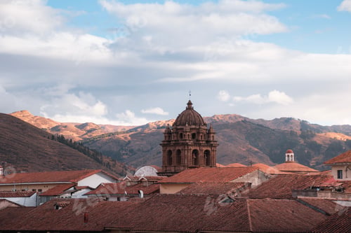 Preview: Church tower emerging from cusco rooftops with andes mountains in background