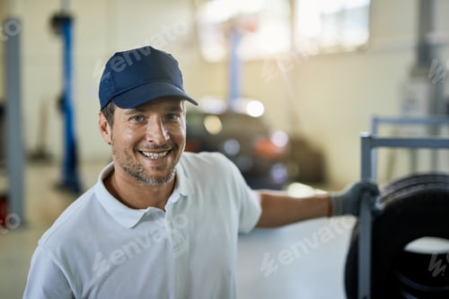 Preview: Happy mechanic pulling rack with car tires in auto repair shop.