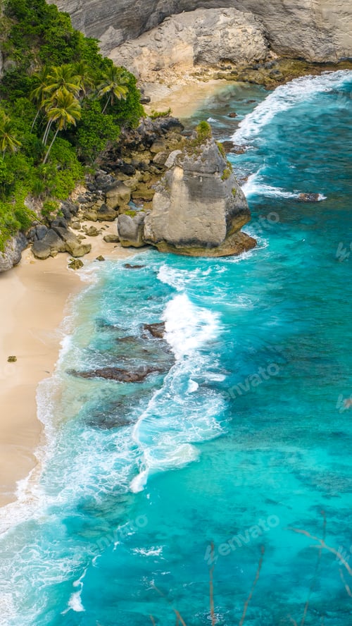 Preview: Rock in the ocean with beautiful palms behind at Atuh beach on Nusa Penida island, Indonesia