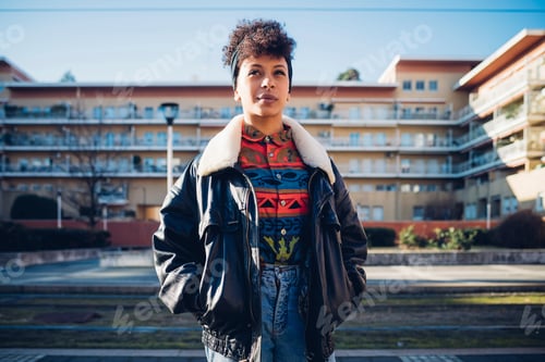 Preview: Cool young woman on urban sidewalk looking up, portrait