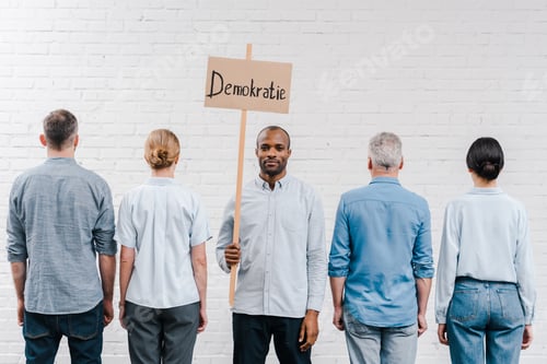 Preview: back view of people standing near brick wall near african american man holding placard with