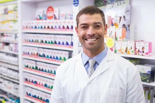 Preview: Male pharmacist standing in pharmacy aisle with medicine boxes wearing coat and tie, copy space