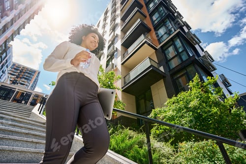 Preview: Smiling curly woman walking down the stairs
