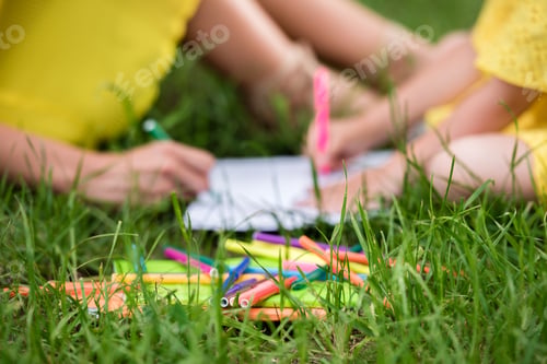 Preview: cropped shot of mother and daughter drawing with felt tip pens while sitting on green grass