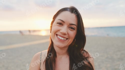 Preview: Young woman opens her eyes and smiles at the camera while standing on the beach
